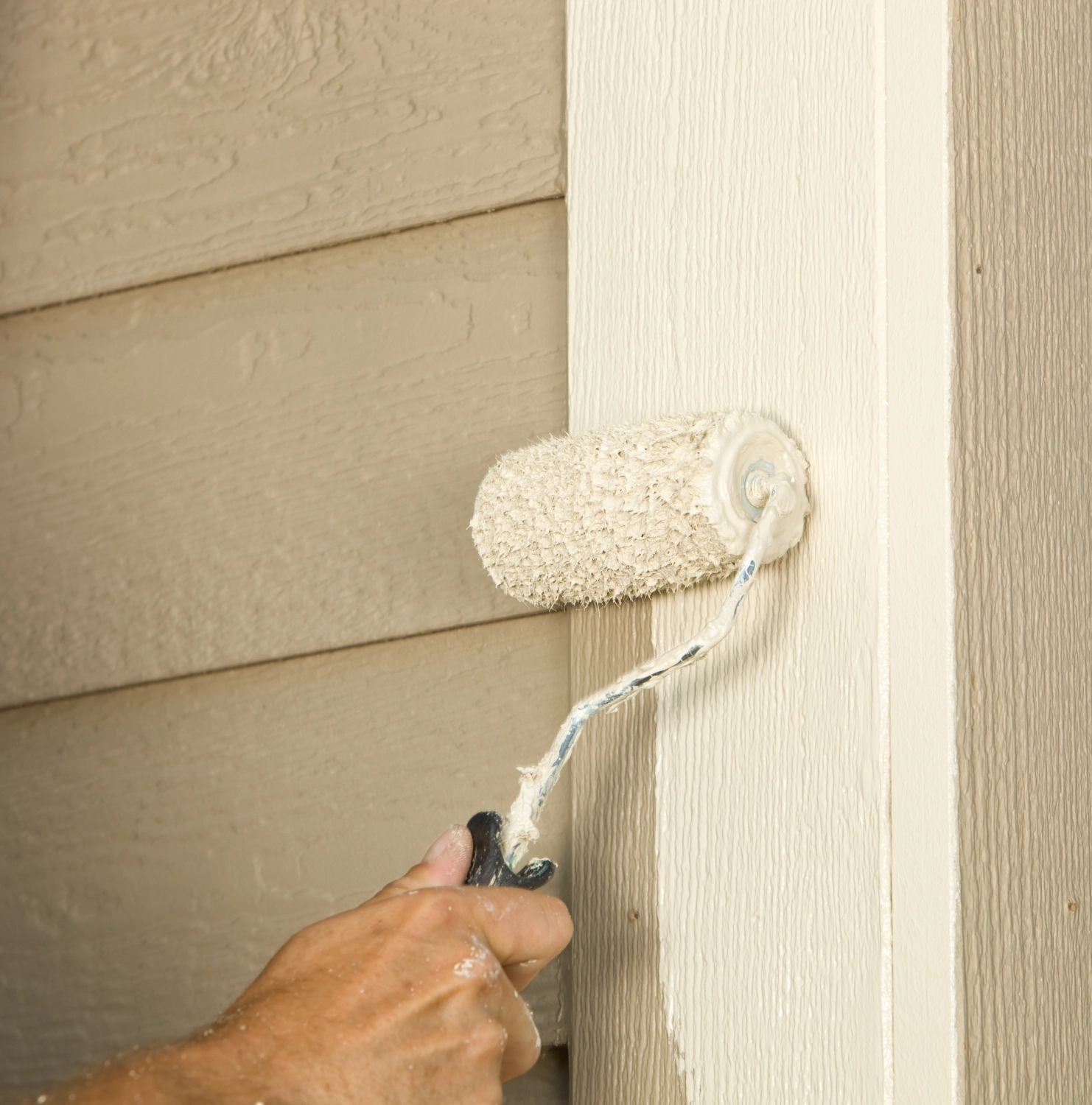 A person paints a beige wall with a paint roller.