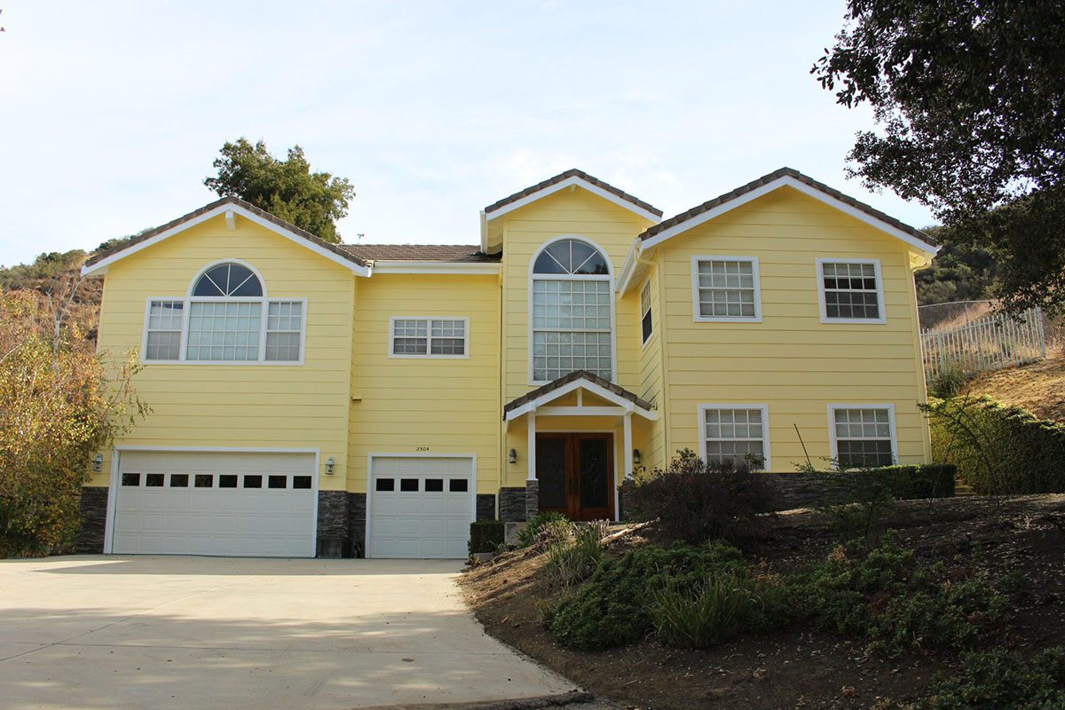 A yellow house with two garage doors and a driveway.