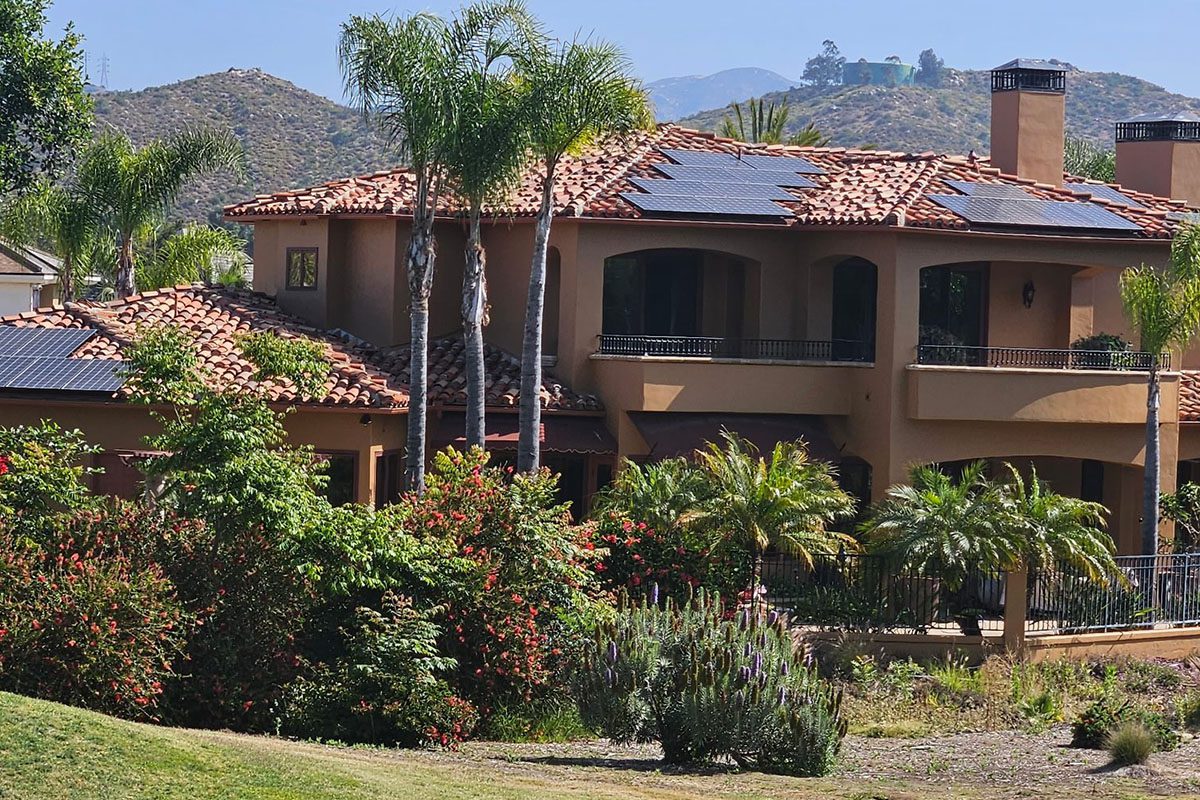 A large brown house with palm trees and bushes.