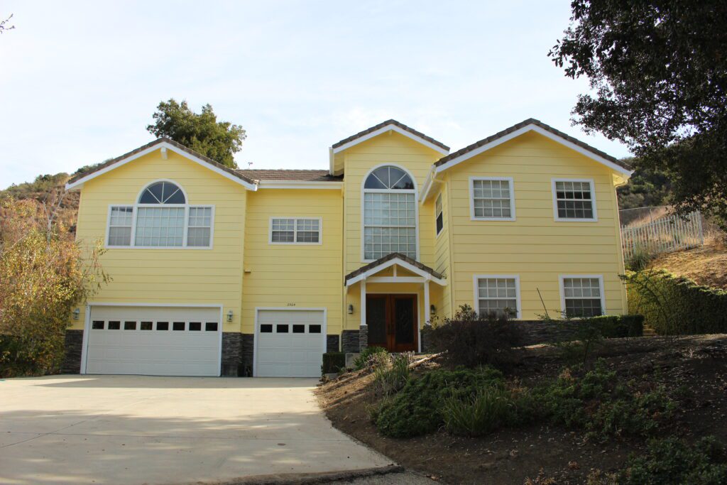 A yellow house with two garage doors and a driveway.
