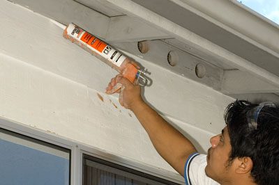A man holding a glue gun and painting the ceiling.